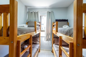 Ein Schlafsaalzimmer mit Etagenbetten, einem Fenster mit Vorhängen und einer Tür, die nach draußen führt.