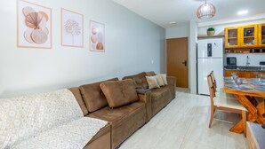 Una sala de estar con sofá, una mesa de comedor con sillas, una zona de cocina con armarios y un refrigerador.