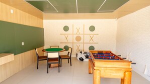 Una habitación con mesa de fútbol, mesa de billar y un juego de tres en raya en la pared.