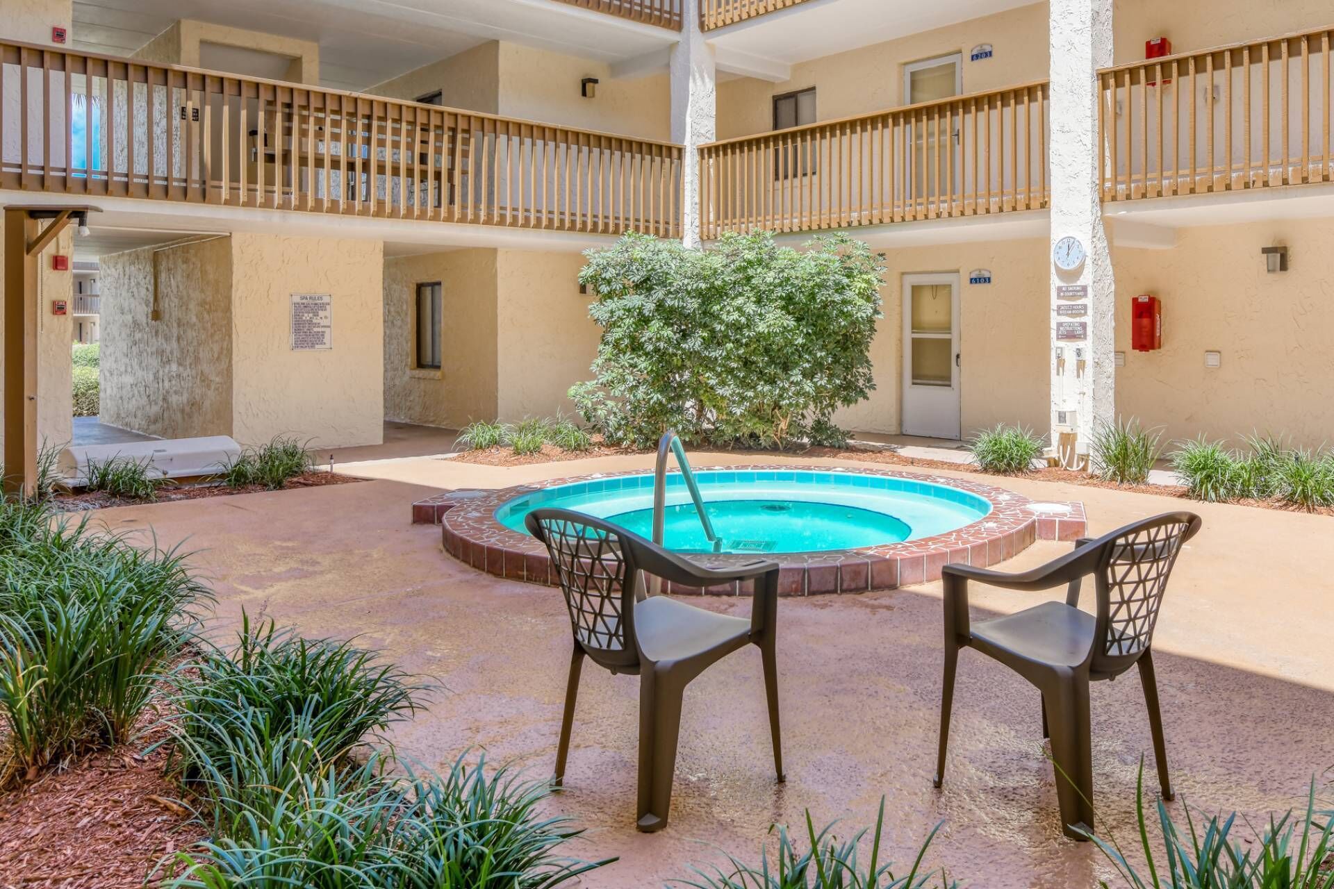 A courtyard with a swimming pool, two chairs, a tree, and a multi-level building.