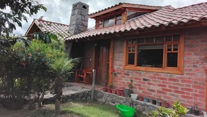 Une maison en briques avec un toit en tuiles, une cheminée et un petit porche avec une chaise.