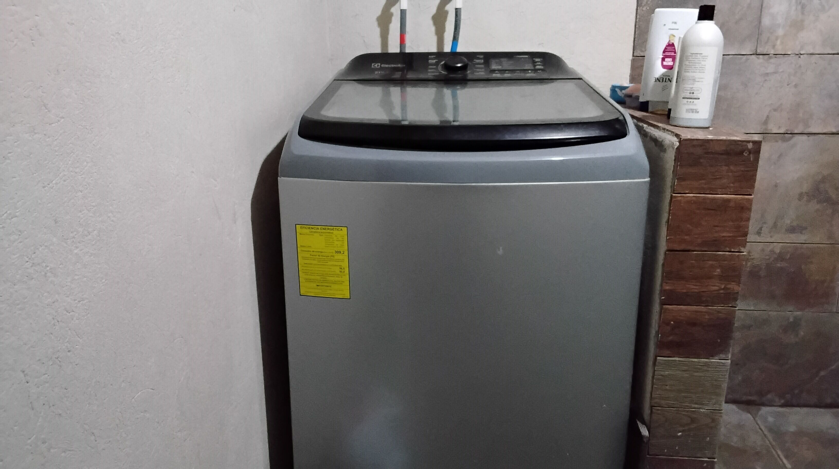 A gray appliance with a yellow sticker, two power cables, and a white bottle on a tiled surface.