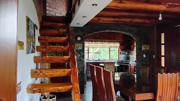 Un intérieur rustique avec un escalier en bois, un coin cuisine doté d’appareils modernes et une vue sur l’extérieur à travers une porte en arc de cercle.