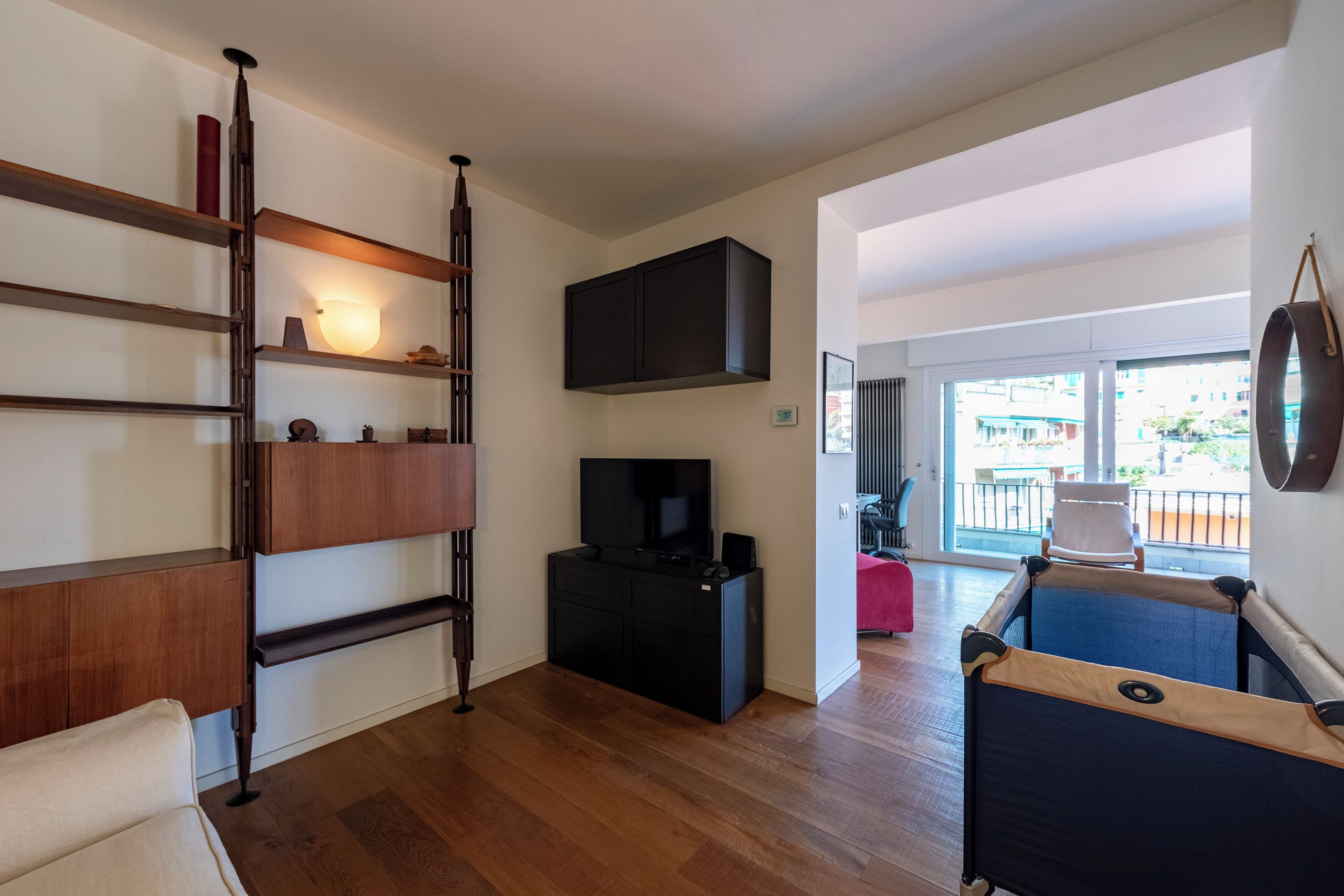 A modern living room with a TV, wooden shelves, and a balcony view.