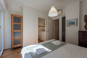 Ein Schlafzimmer mit Bett, einem Holzschrank, einem durchgehenden Türbogen erkennbaren Badezimmer und einer Hängeleuchte.