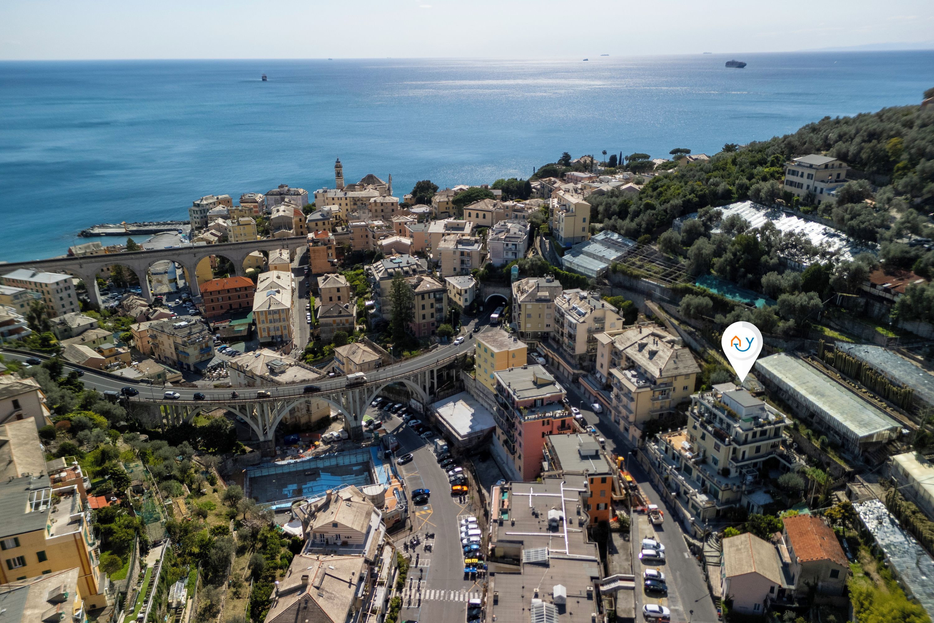 An aerial view of a coastal town with a prominent bridge, dense buildings, and a clear view of the sea.