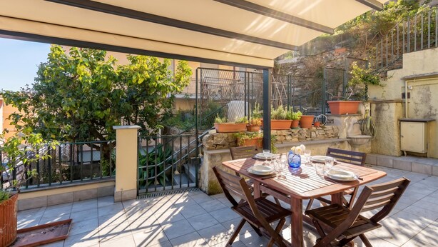 Un patio al aire libre con una mesa lista para comer, rodeado de plantas en macetas y un muro de piedra.