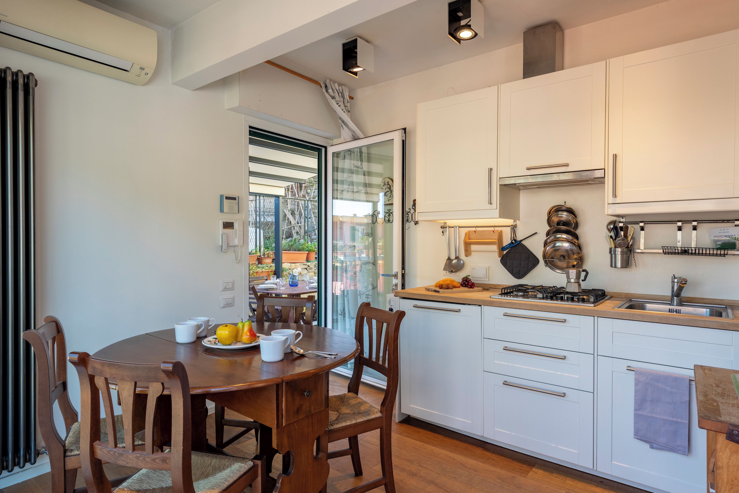 Una cocina moderna con armarios blancos, una mesa de comedor con sillas y vistas a un espacio exterior a través de un ventanal.