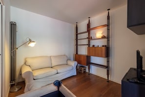 Ein Wohnzimmer mit einer Couch, einer Stehlampe, einem TV-Schrank und einer Holzregaleinrichtung.