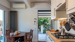Una cocina moderna con estufa a gas, armarios blancos y un comedor con mesa y sillas de madera.