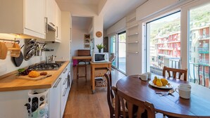 Una cocina moderna con encimera de madera, una mesa de comedor con sillas, vistas a edificios a través de amplios ventanales y un televisor pequeño sobre un mueble.
