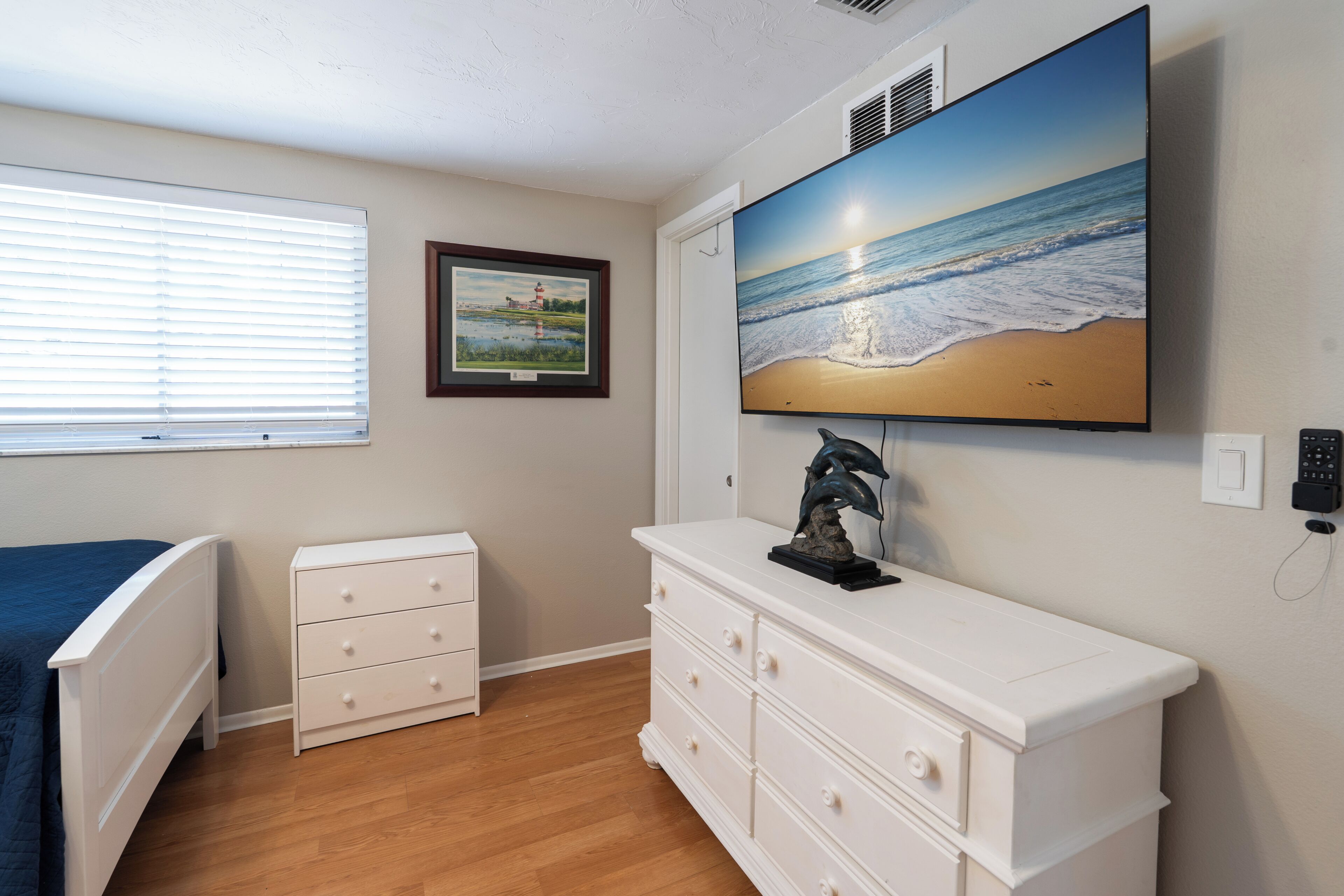 A bedroom with a bed, a dresser, a TV, and a window with blinds.