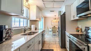 Una cucina moderna con elettrodomestici in acciaio inossidabile, mobili bianchi e un'area pranzo con un lampadario.