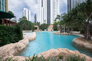 A swimming pool with rock formations, palm trees, and a slide. - Coastal View Haven with Balcony (Gold Coast)
