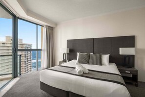 A hotel room with a large bed, a nightstand, a lamp, and a view of the ocean. - Coastal View Haven with Balcony (Gold Coast)