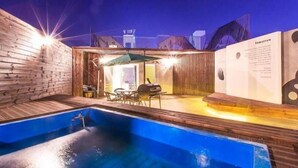 Uma piscina com um deck de madeira, área de churrasco e um espaço coberto para sentar.
