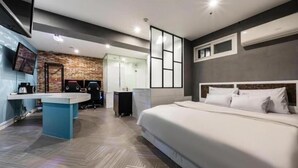 Quarto de hotel moderno com uma cama grande, uma escrivaninha com cadeiras, uma televisão e uma parede de tijolos.