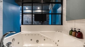 Um banheiro moderno com uma banheira grande, uma janela com vista para uma parede de tijolos e um conjunto de produtos de higiene pessoal na parede.