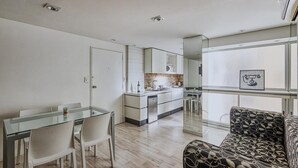 Et moderne køkken med en central ø, et spiseområde med et glasbord og en sofa med et mønster.