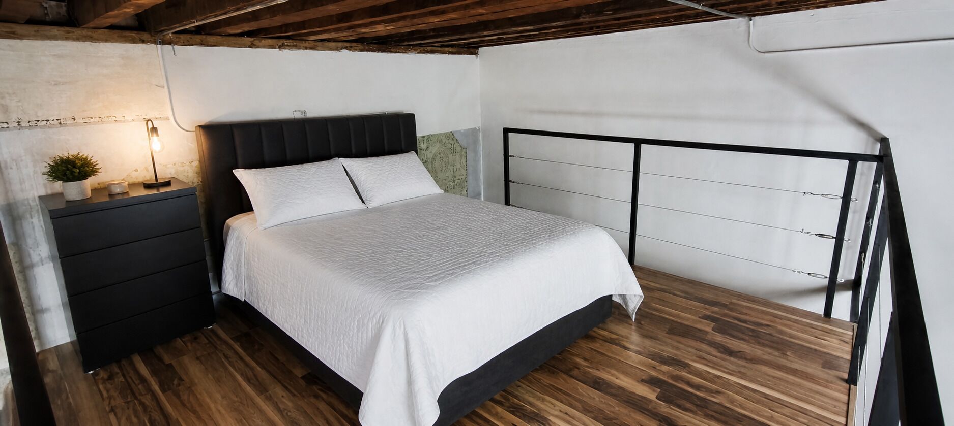 Une chambre à coucher avec un lit, une table de chevet, une lampe et un plancher en bois.