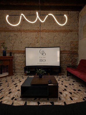 A living room with a stone wall, a TV, a red sofa, and a coffee table with a plant. - CASA BO | LOFT IN THE HEART OF MEXICO CITY (Ciudad de México)