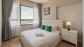 A hotel room with a large bed, a nightstand with a lamp, a view of the city through the window, and a painting on the wall. - Nice stay next to Thao Dien area, 3brs, 5min to MRT, central (Thành phố Hồ Chí Minh)