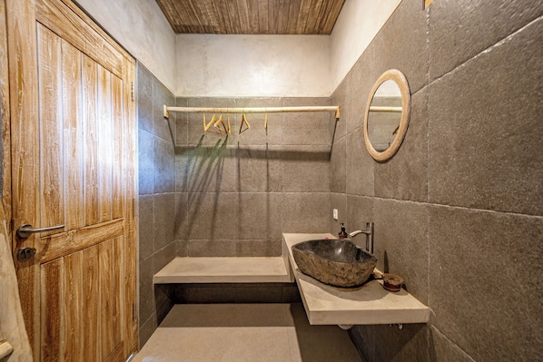 A bathroom with a wooden door, a stone sink, a mirror, and a towel rack.