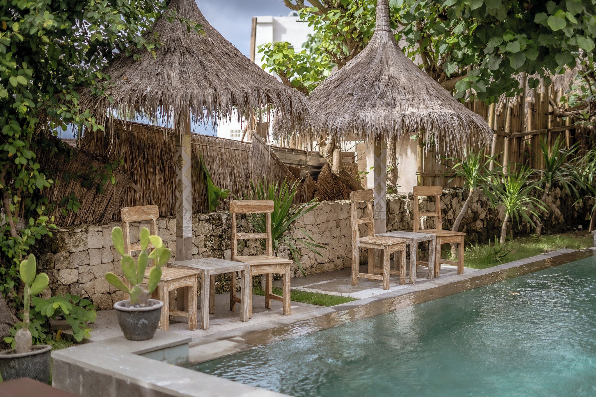 A poolside area with thatched umbrellas, wooden chairs, and potted plants.