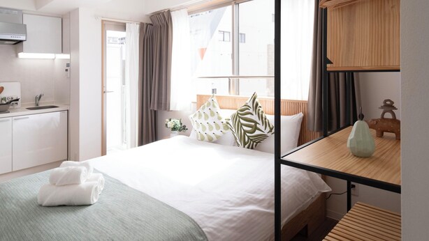 Ein modernes Hotelzimmer mit Bett, einer kleinen Küchenzeile, einem Holzregal und einem großen Fenster.