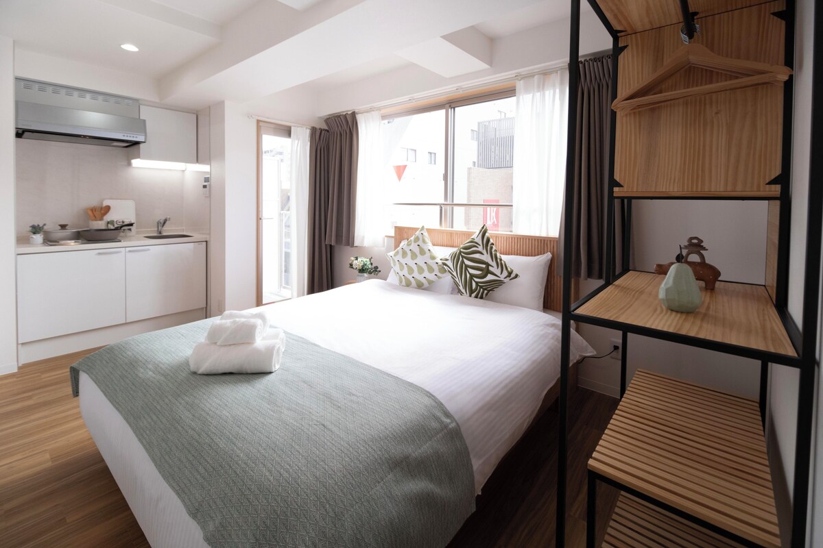 Ein Hotelzimmer mit einem Bett, einer Küchenzeile, einem Holzregal und einem Fenster mit Vorhängen.