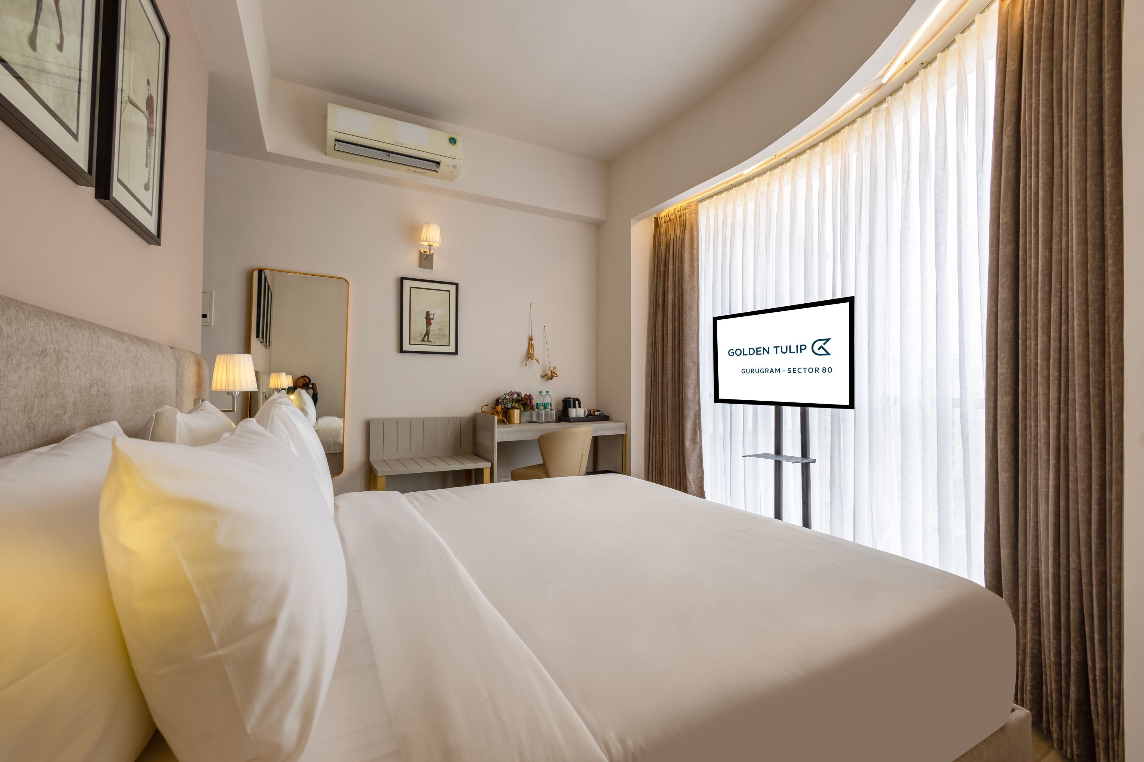 Een hotelkamer met een bed, bureau, stoel en een televisiescherm waarop 'GOLDEN TULIP' staat.