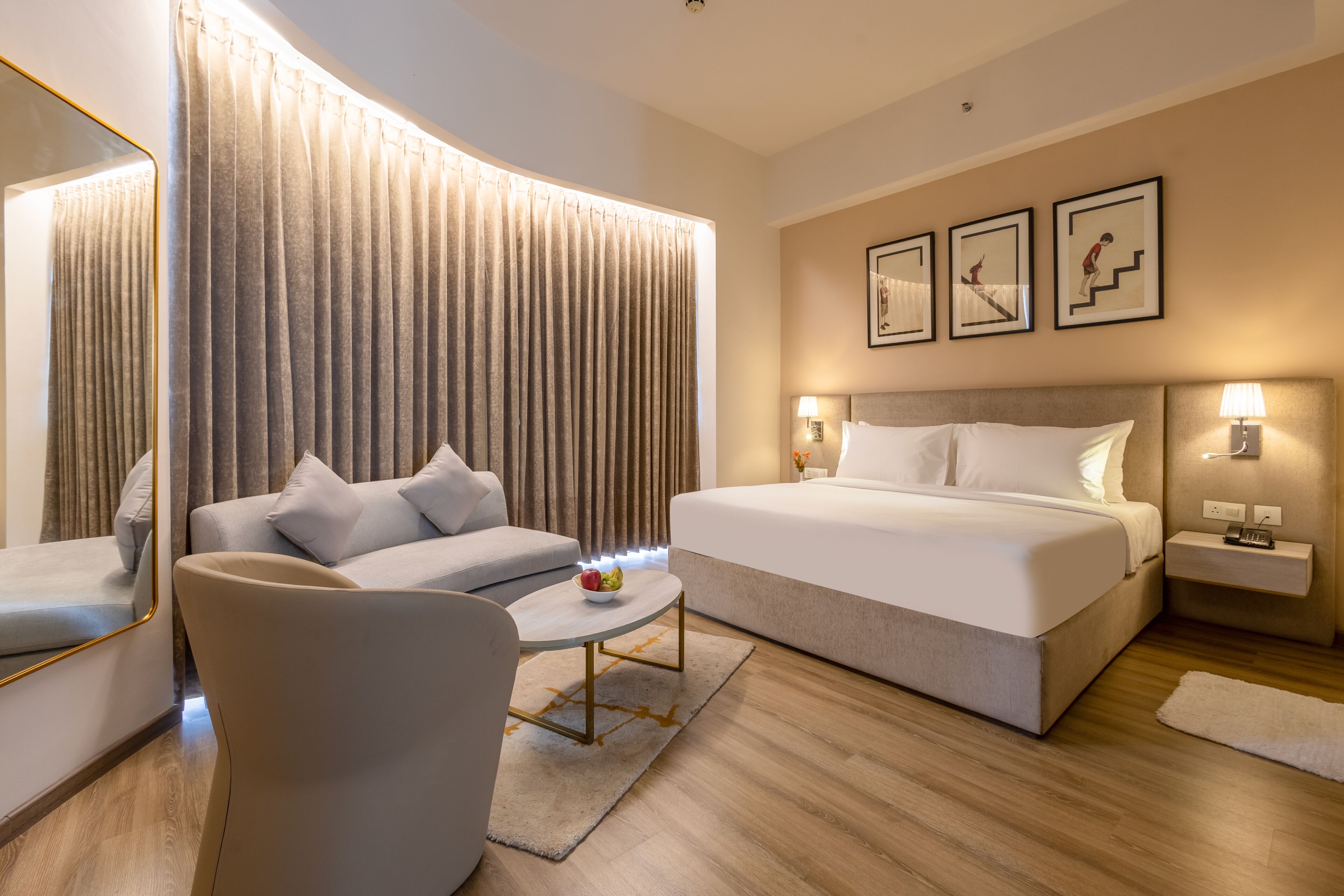 Quarto de hotel moderno com uma cama, um sofá, uma pequena mesa com frutas e um espelho.