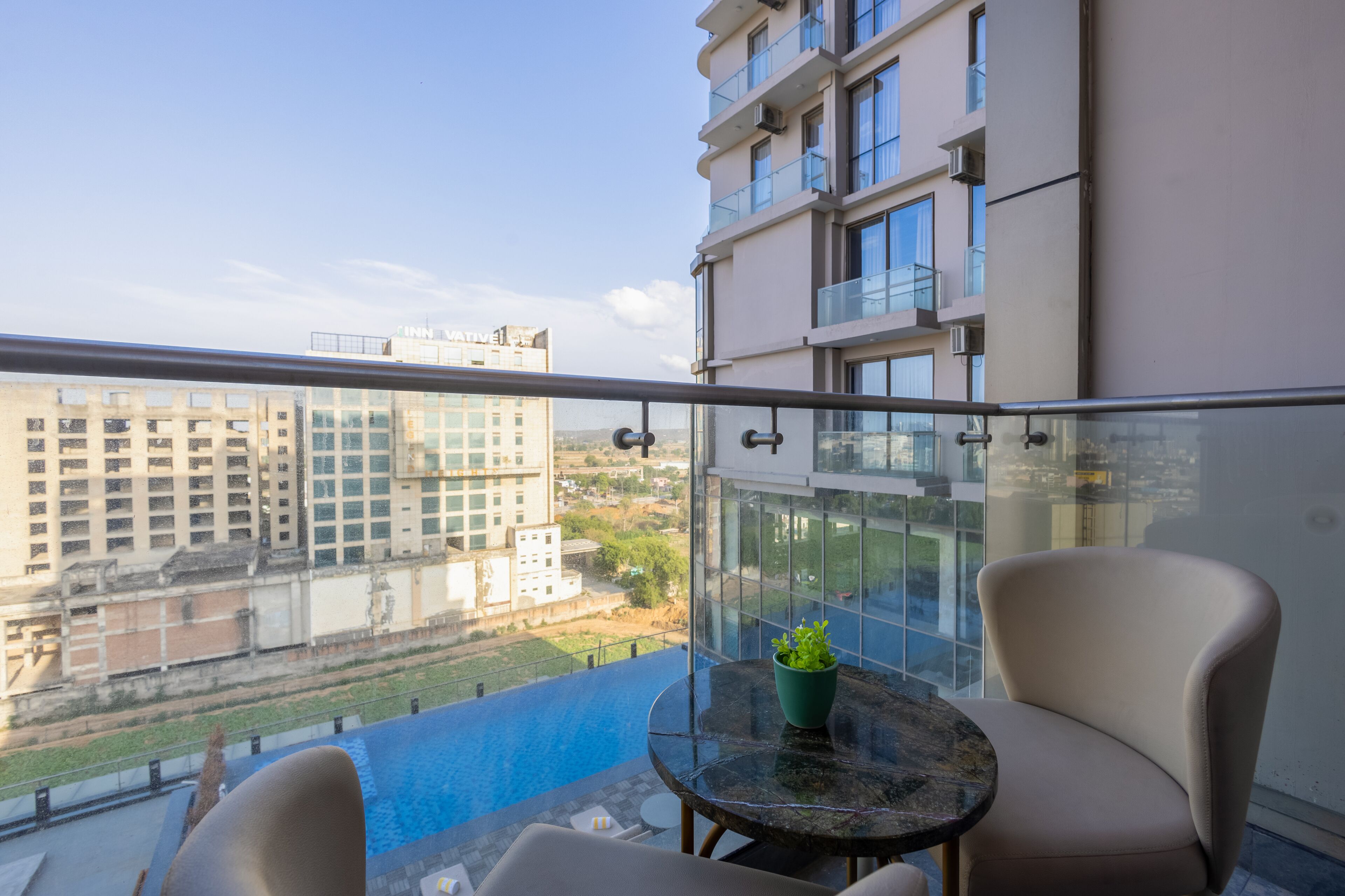 A balcony with a glass railing, a table with a potted plant, and two chairs.
