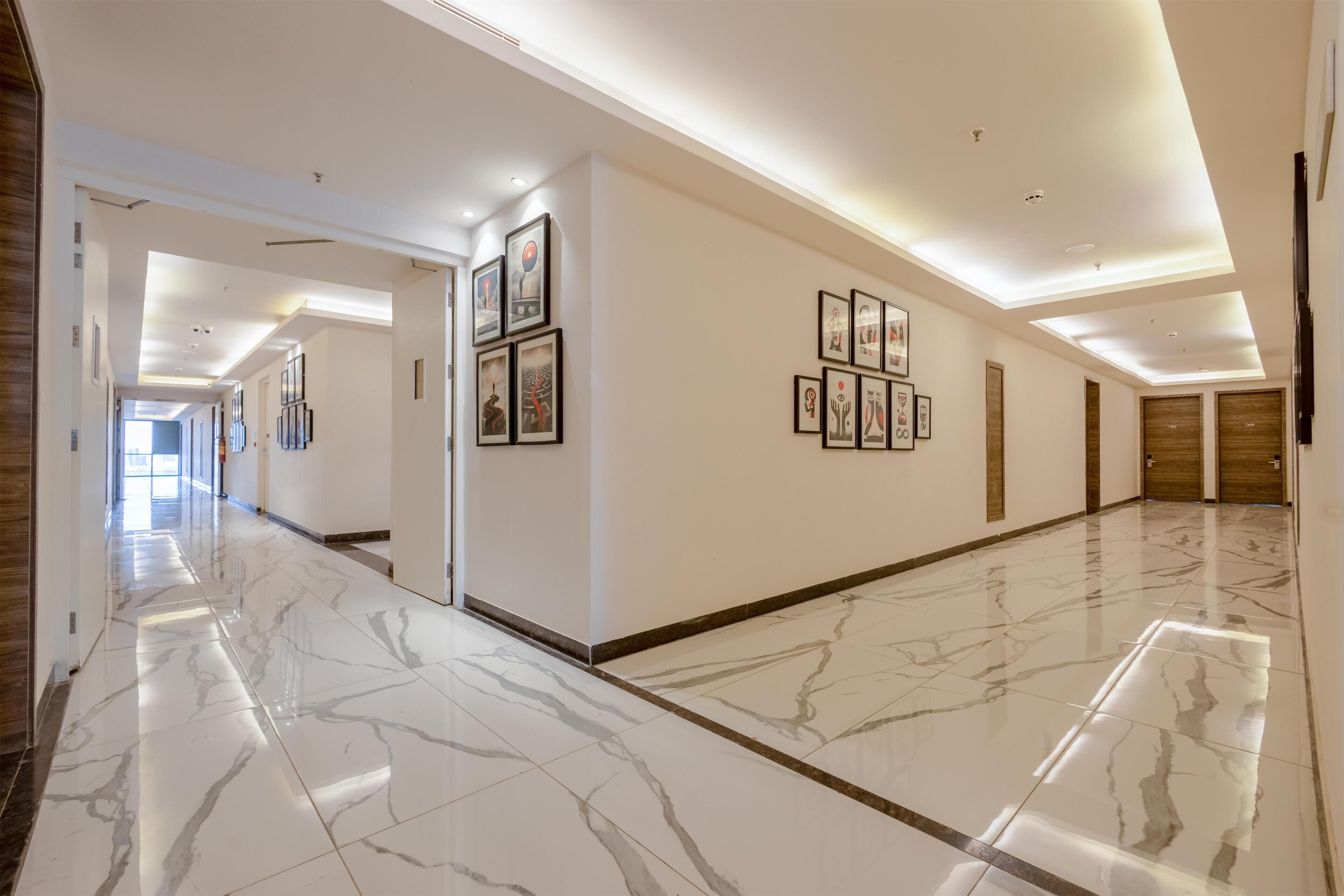A hotel corridor with marble flooring, framed artwork on the walls, and wooden doors at the end.