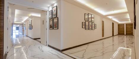 A hotel corridor with marble flooring, framed artwork on the walls, and wooden doors at the end.