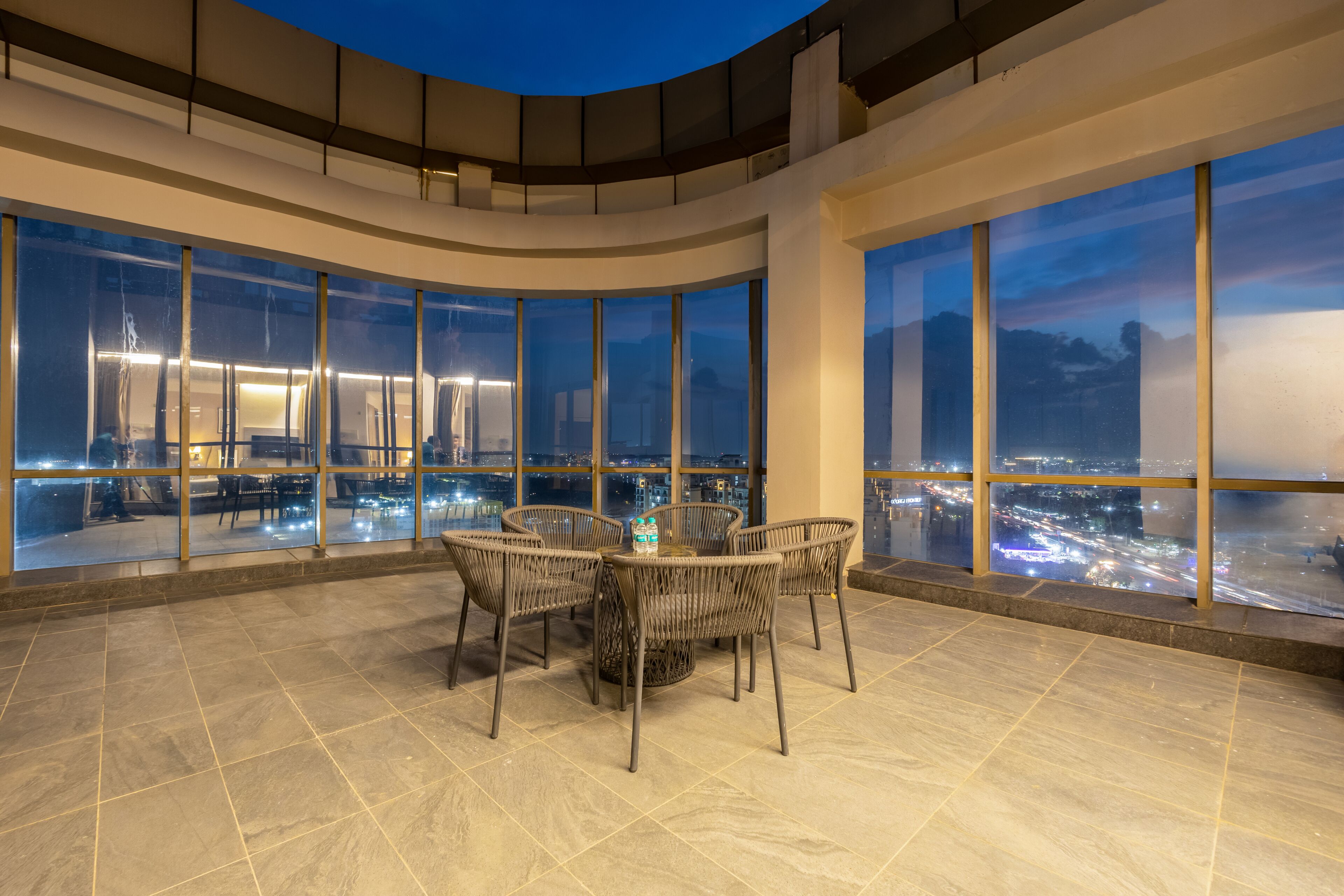 A spacious terrace with a round table and chairs, large windows offering a city view, and a modern architectural design.