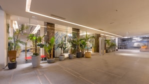 Een moderne hotellobby met een glazen wand, potplanten en een betegelde vloer.