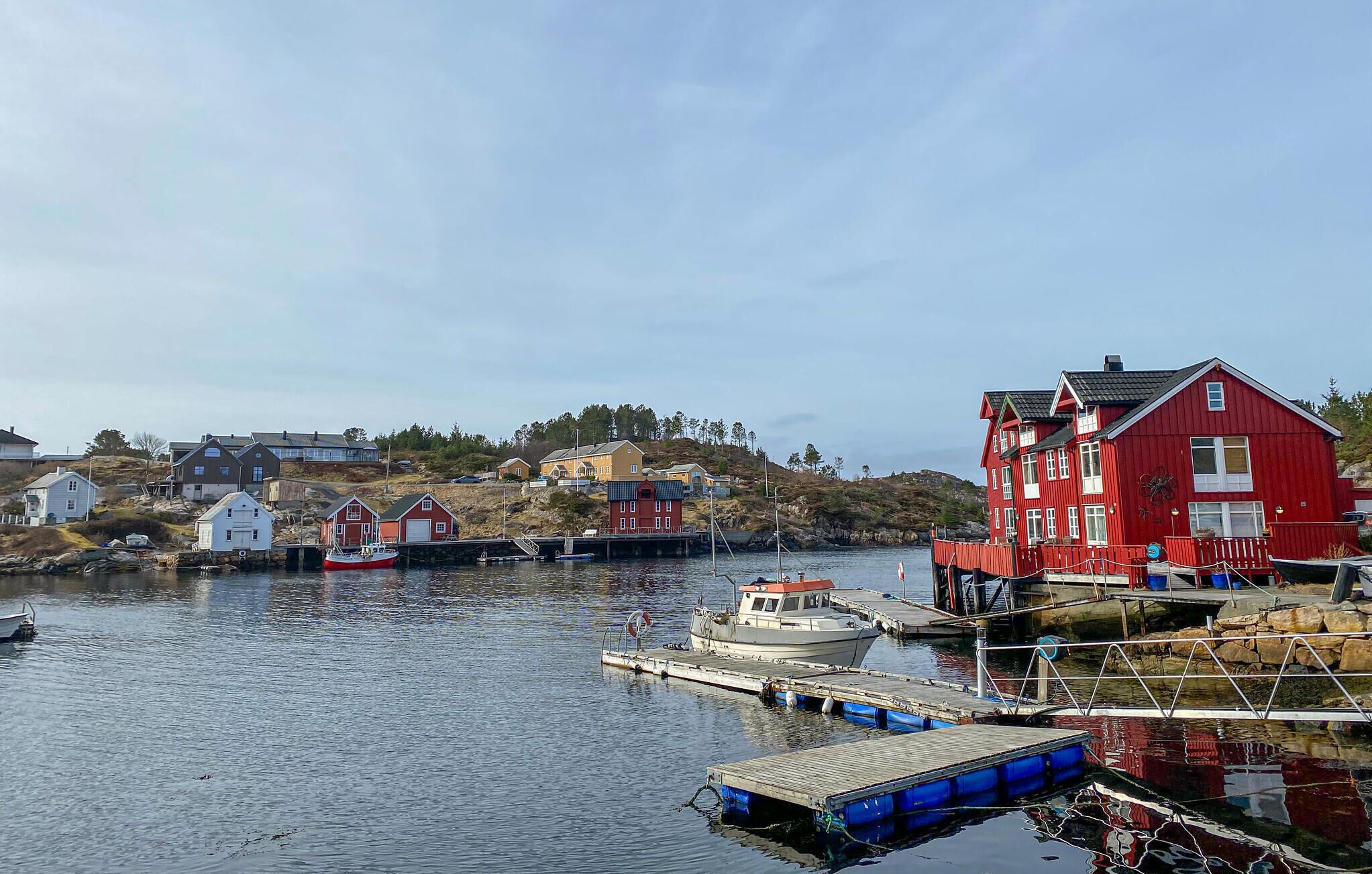 A coastal village with a prominent red building, a dock with boats, and a hilly backdrop.