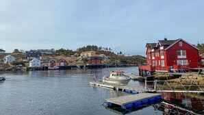 A coastal village with a prominent red building, a dock with boats, and a hilly backdrop.