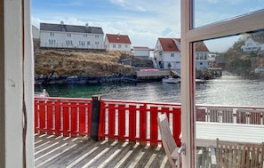 A wooden deck with a red railing, overlooking a calm water body with houses in the background. - 2 bedroom beautiful home in Averøy (Averøy)