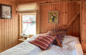 A wooden cabin bedroom with a bed, a sailboat model, a framed picture, and a window view. - 2 bedroom beautiful home in Averøy (Averøy)