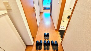 A hallway with wooden flooring, a set of black slippers, and a glimpse of a bathroom with a bathtub and a towel rack. - Gold Mansion Apartments (Tokyo)