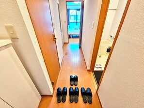 A hallway with wooden flooring, a set of black slippers, and a glimpse of a bathroom with a bathtub and a towel rack. - Gold Mansion Apartments (Tokyo)