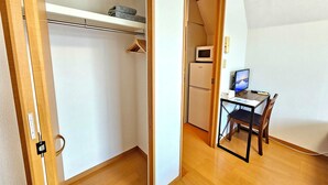 A compact room with a wooden floor, a desk with a computer, a chair, a microwave, and a refrigerator. - Gold Mansion Apartments (Tokyo)