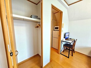 A compact room with a wooden floor, a desk with a computer, a chair, a microwave, and a refrigerator. - Gold Mansion Apartments (Tokyo)
