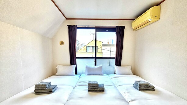 A hotel room with a large bed, two pillows, and a window with curtains. - Gold Mansion Apartments (Tokyo)