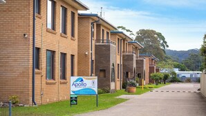 A row of brick buildings with a sign for Apollo Holiday Units, indicating a 5-minute walk to the speedway. - Apollo Holiday Units (Narooma)
