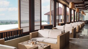 A modern lounge area with wicker furniture, large windows, and a view of the cityscape. - Kamala Bali Resort by AGATA (Nusa Dua)