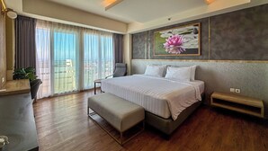 A modern hotel room with a large bed, a desk, a chair, and a balcony with curtains. - Kamala Bali Resort by AGATA (Nusa Dua)