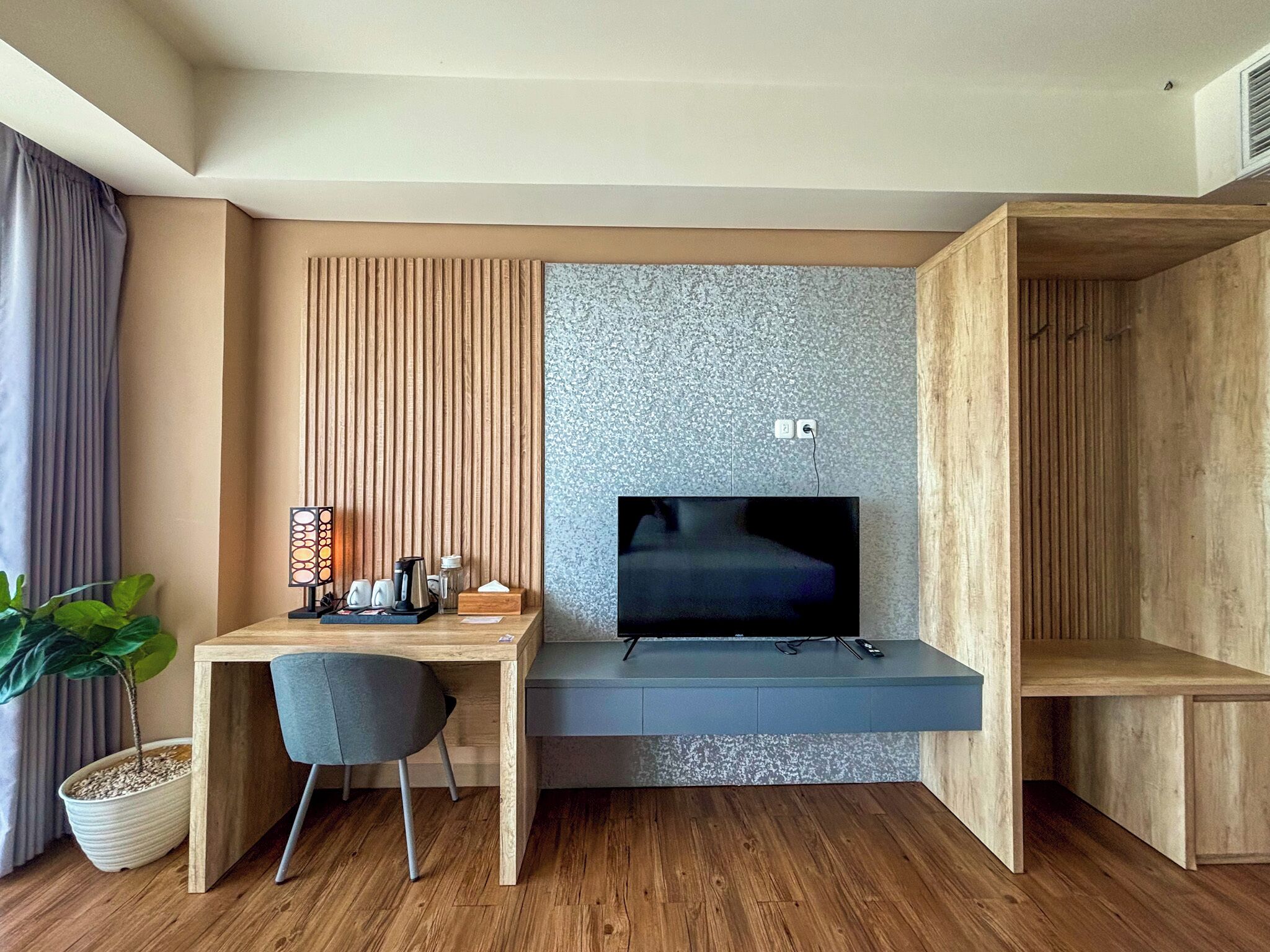 A modern room with a wooden desk, a chair, a TV, and a potted plant.